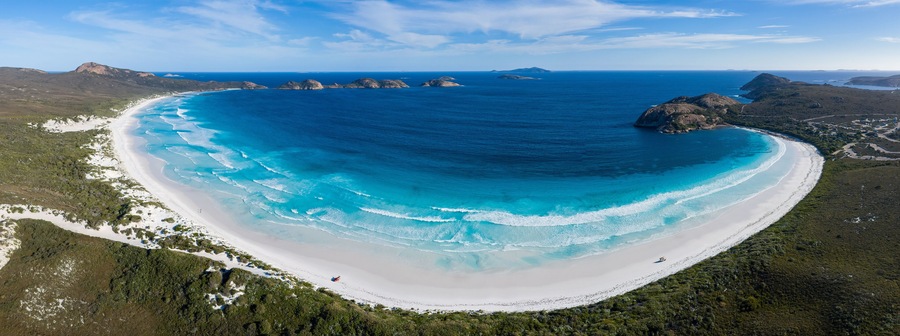 A coastal landscape with a white sandy beach, clear blue waters, and green vegetation.