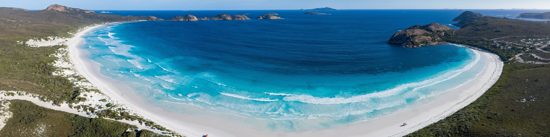 A coastal landscape with a white sandy beach, clear blue waters, and green vegetation.