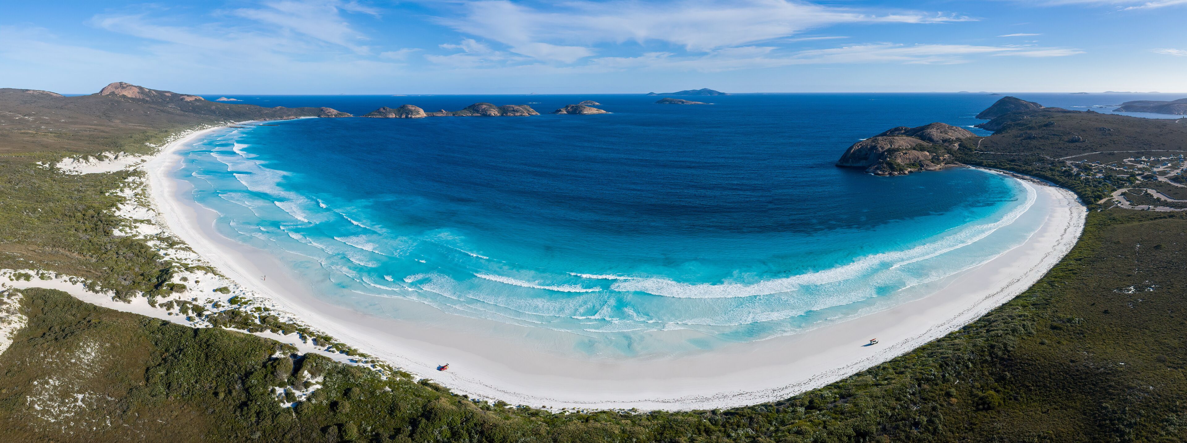 A coastal landscape with a white sandy beach, clear blue waters, and green vegetation.