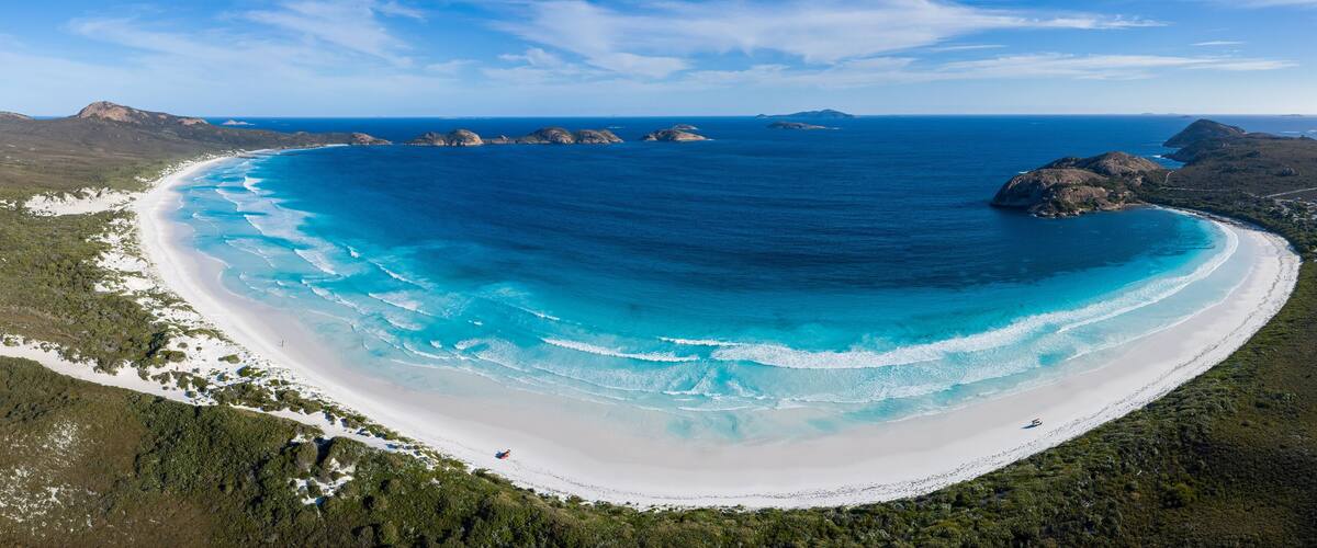 A coastal landscape with a white sandy beach, clear blue waters, and green vegetation.