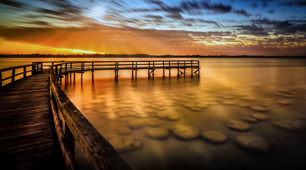 A wooden pier extending into calm water at sunset with a clear sky.