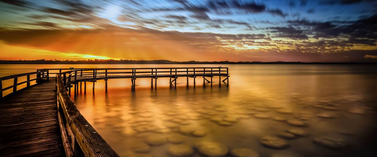 A wooden pier extending into calm water at sunset with a clear sky.
