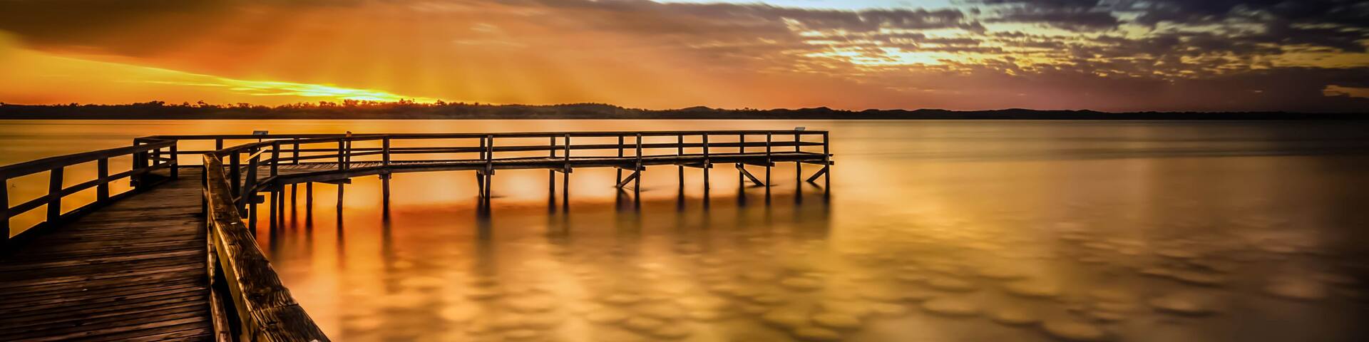 A wooden pier extending into calm water at sunset with a clear sky.