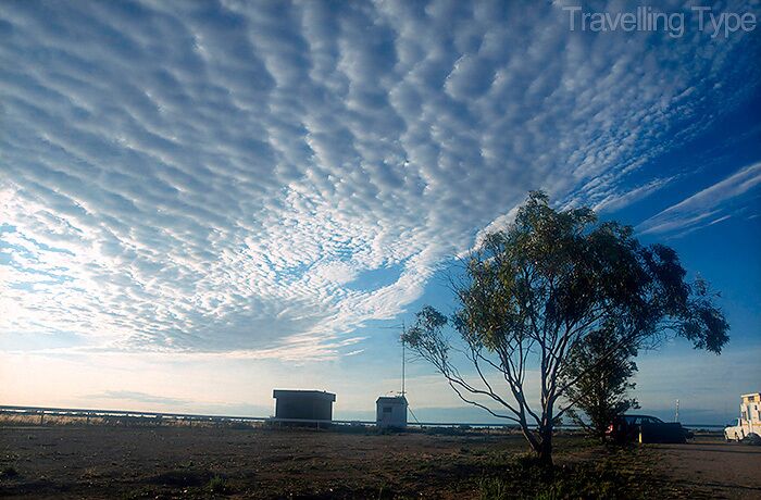 A landscape with a tree, a building, and a clear sky with clouds.