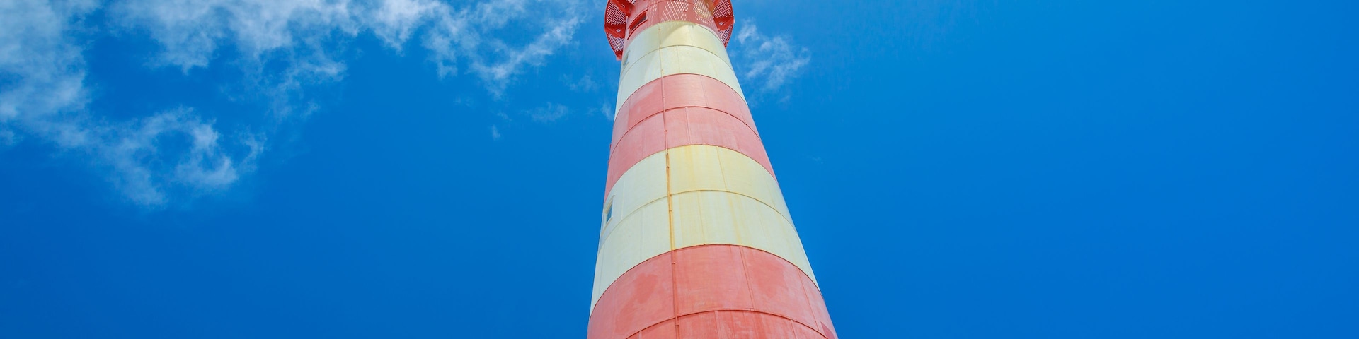 Un faro alto y a rayas contra un cielo azul despejado.