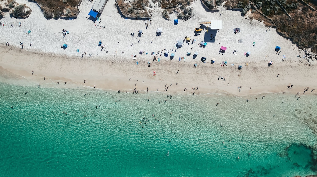 Vista aérea de una playa con aguas turquesas transparentes, gente tomando el sol y sombrillas de playa.