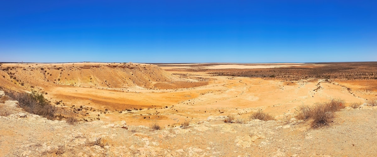 Un vaste paysage désertique, avec des collines douces et une végétation clairsemée.