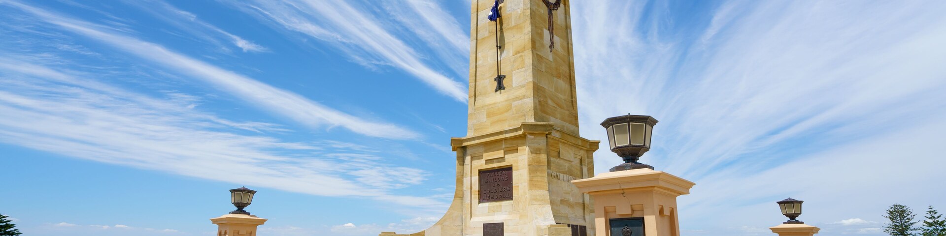 Un monumento alto con un reloj, rodeado de escalones y dos faroles.
