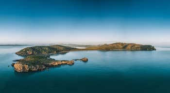 A coastal landscape with a large island surrounded by calm blue waters, featuring rocky outcrops and dense greenery.