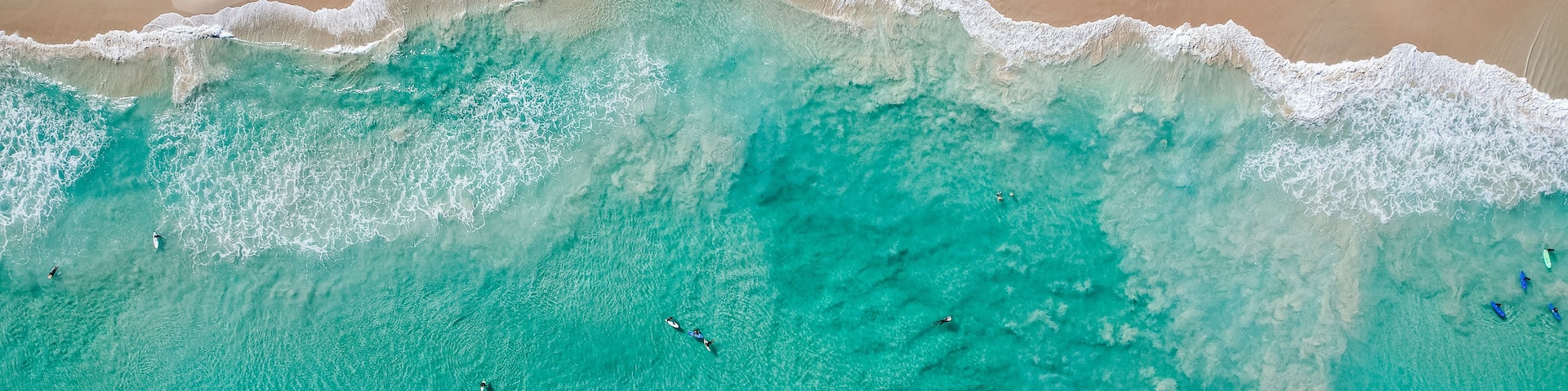 Océano turquesa con olas rompiendo sobre una playa de arena.