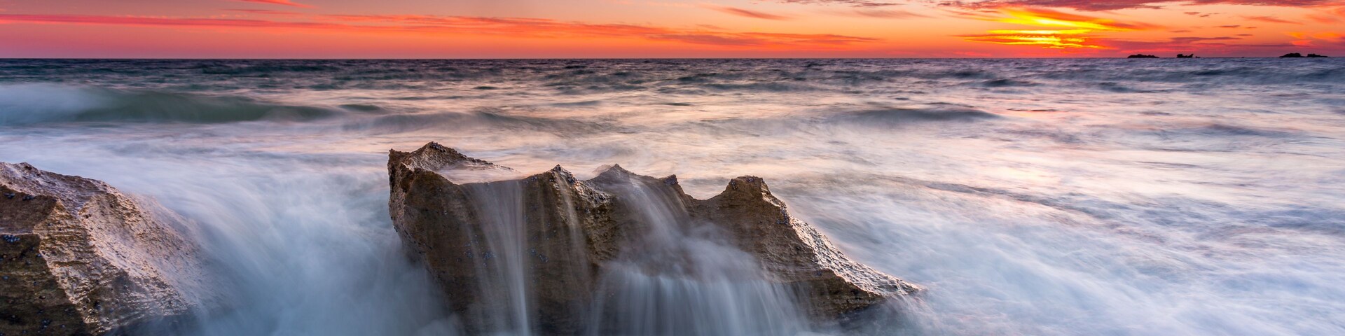 Un atardecer sobre el océano con un promontorio rocoso al frente.