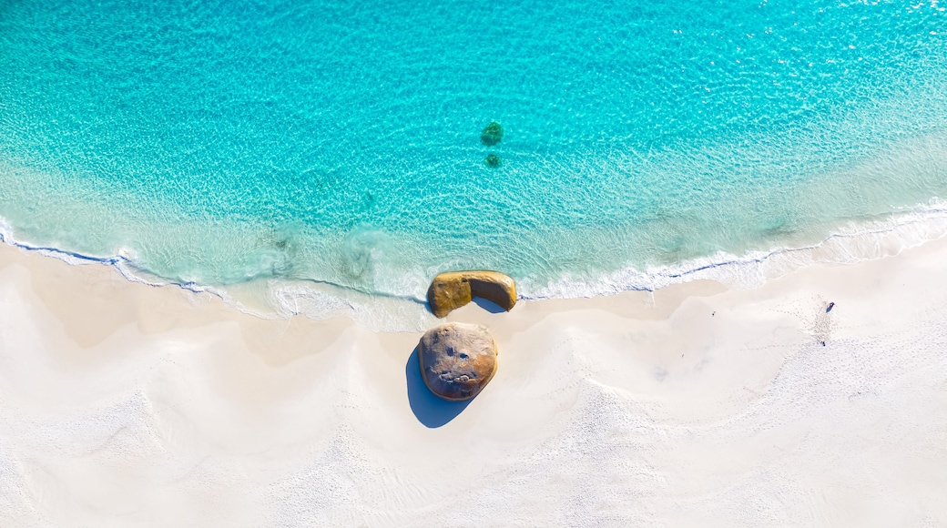 A beach with clear turquoise water, white sand, and two large rocks.