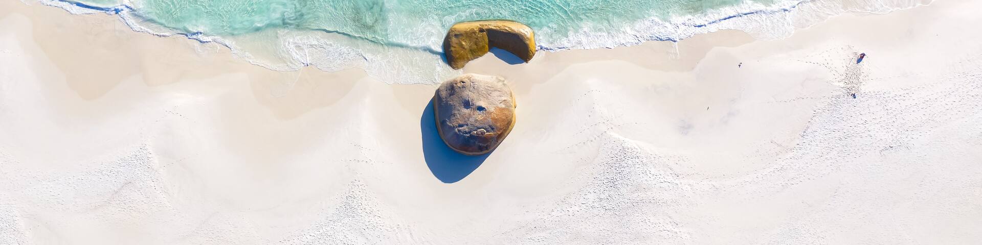 A beach with clear turquoise water, white sand, and two large rocks.