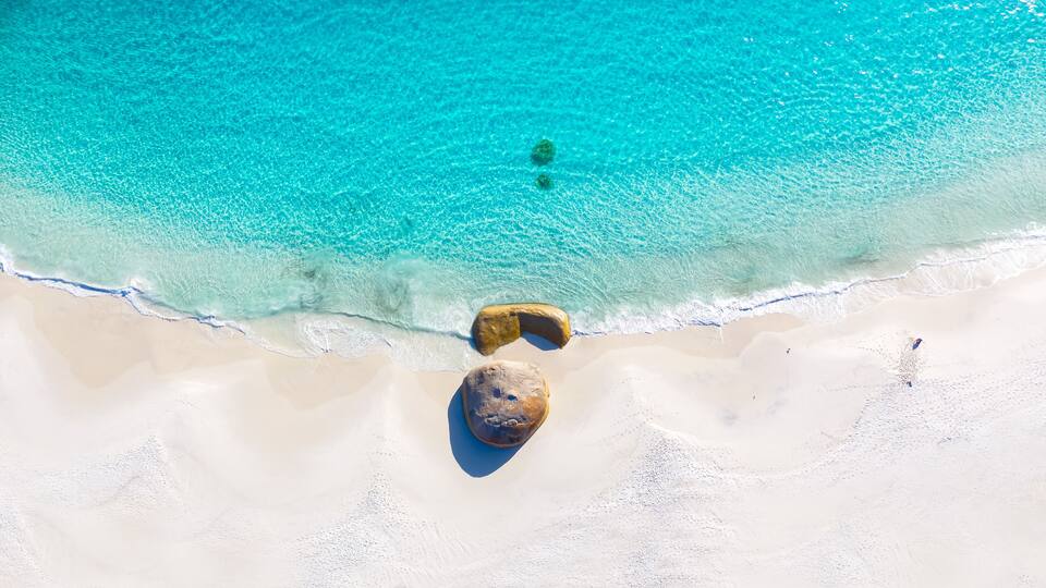 A beach with clear turquoise water, white sand, and two large rocks.