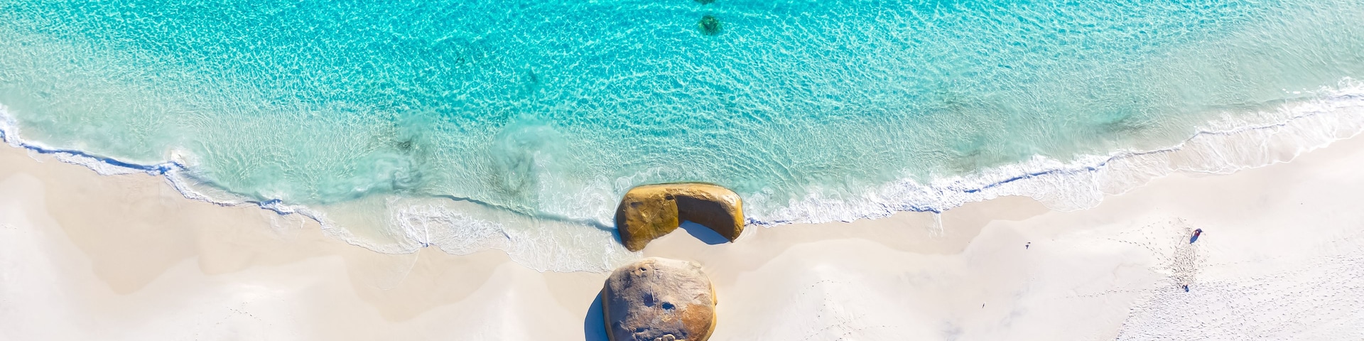 Uma praia com águas turquesa cristalinas, areia branca e duas grandes rochas.
