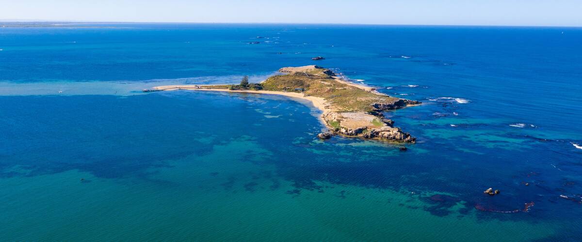 An aerial view of a coastal island with clear blue waters, sandy beaches, and rocky outcrops.