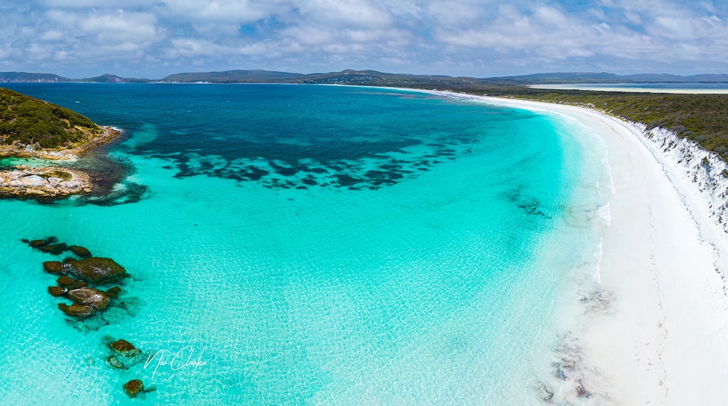 A turquoise sea with white sandy beaches, rocky outcrops, and distant mountains.