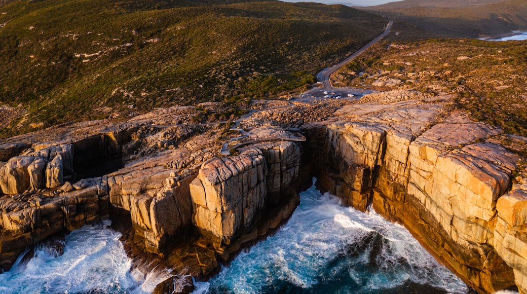 A coastal landscape with rocky cliffs, a winding road, and a distant view of hills.