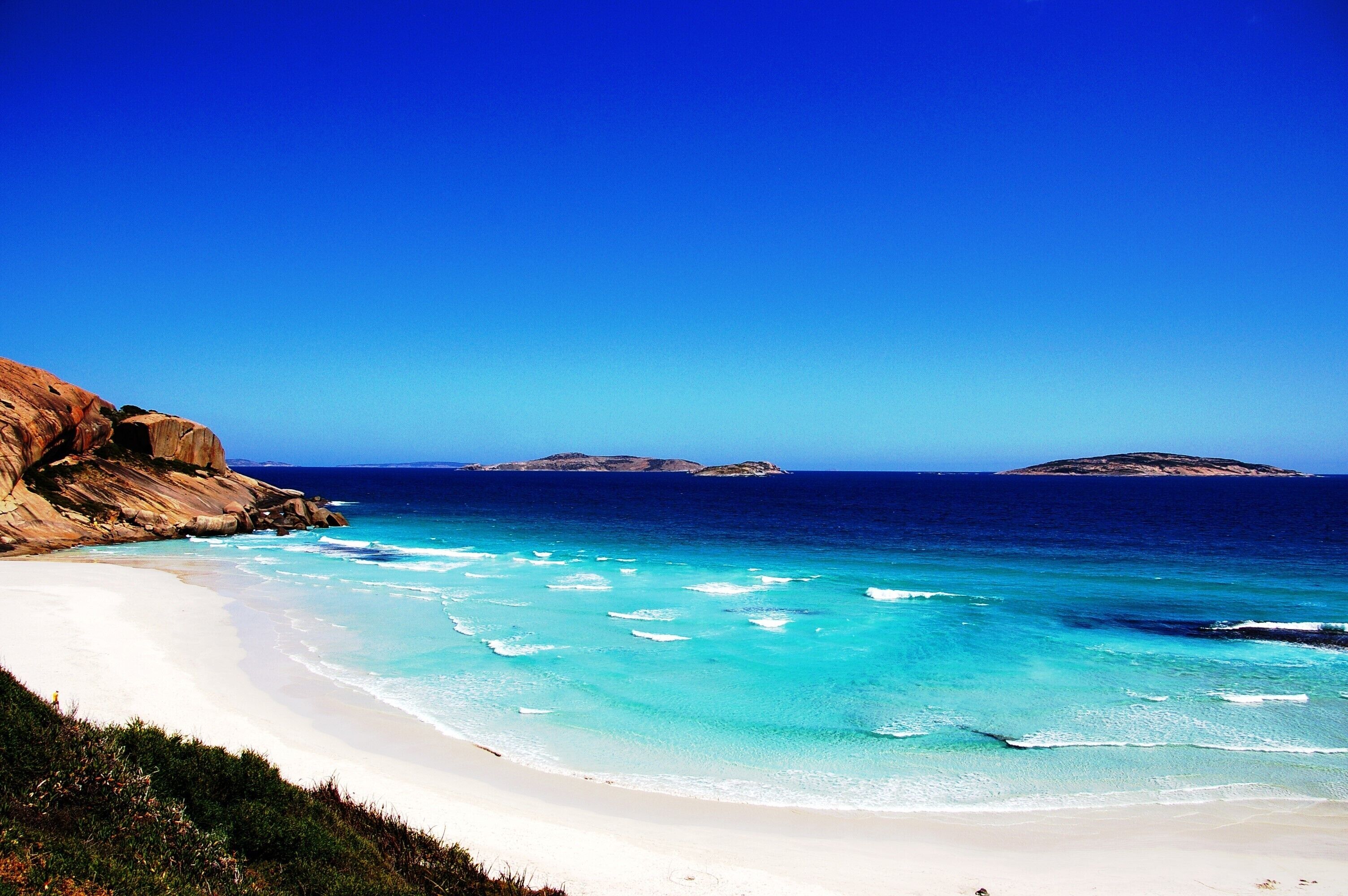 A beach with clear turquoise waters, white sand, and rocky cliffs.