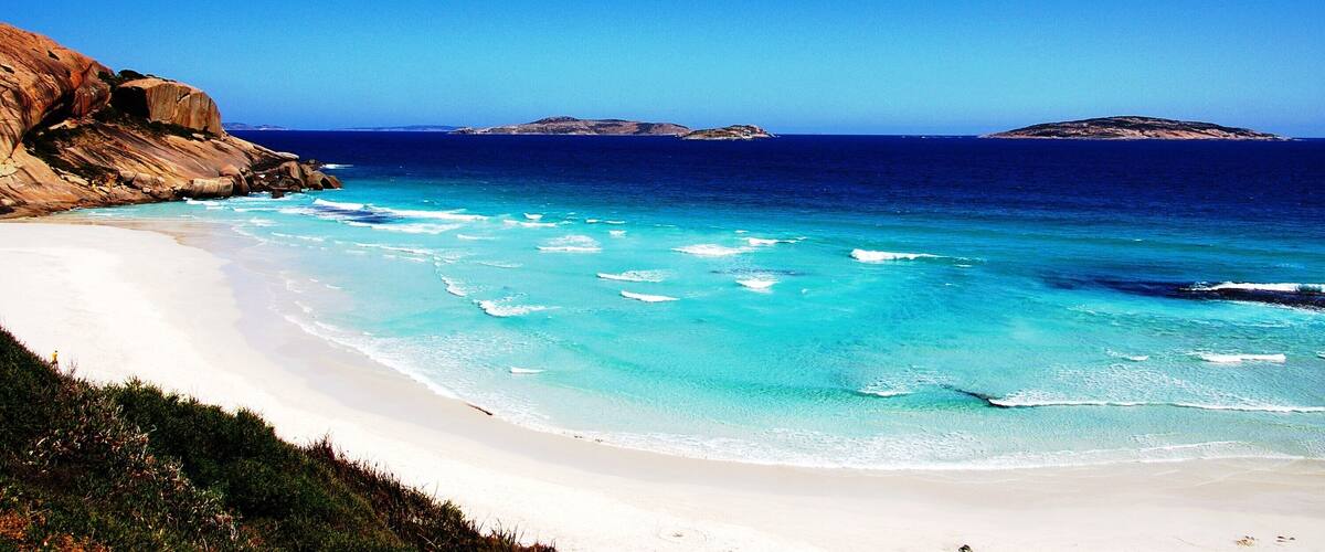 A beach with clear turquoise waters, white sand, and rocky cliffs.
