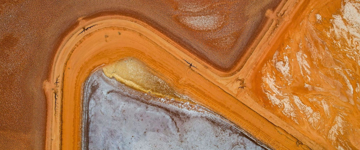 Eine Vogelperspektive zeigt eine Landschaft mit einer großen Wasserfläche, einem deutlichen orangefarbenen Bereich und einem weißen Bereich mit einem gelben Fleck.