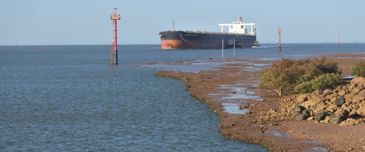 A large cargo ship anchored near a rocky shoreline with calm water.