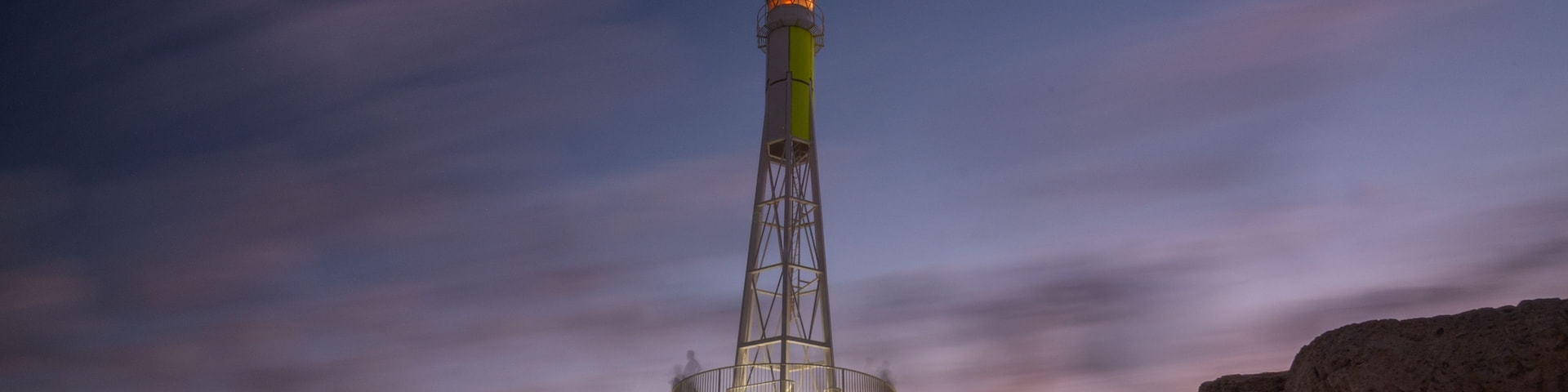 Un faro al atardecer con cielo despejado y primer plano rocoso.