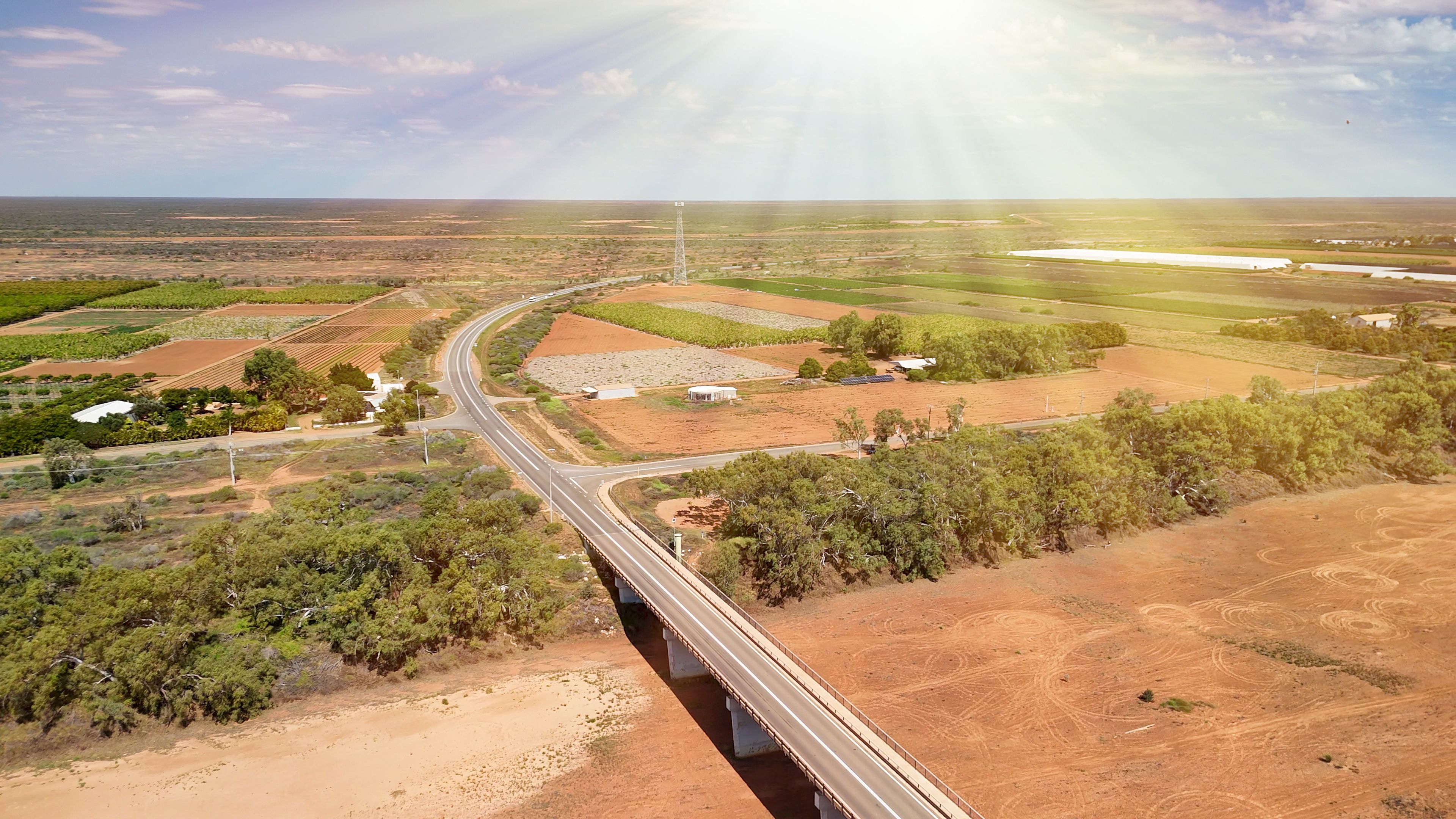 A bridge over a winding road, surrounded by agricultural fields and sparse vegetation.