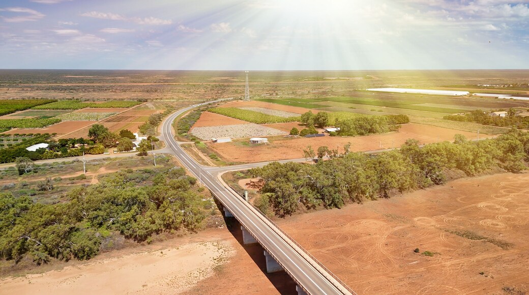 A bridge over a winding road, surrounded by agricultural fields and sparse vegetation.