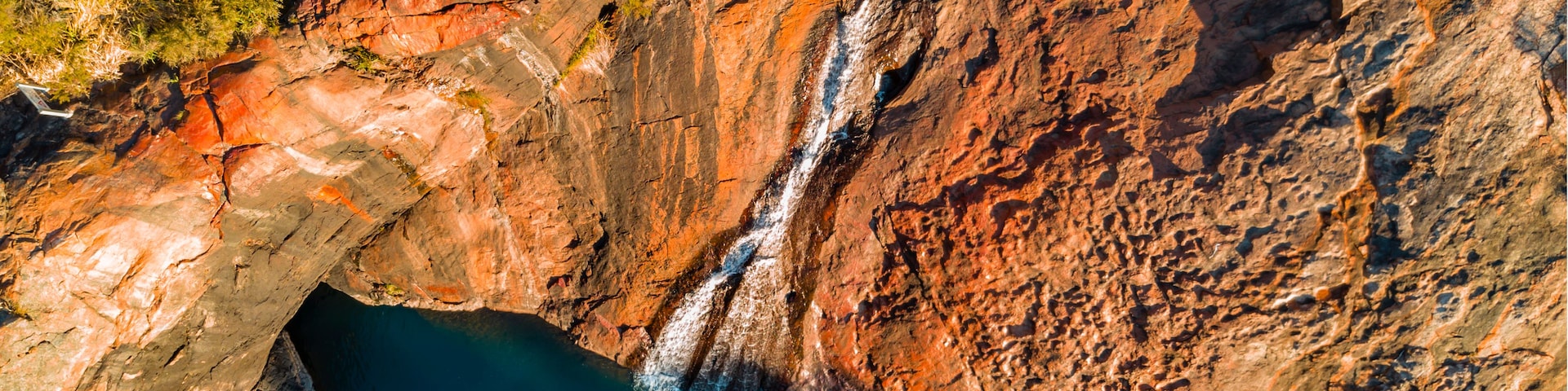 A waterfall cascading down a rocky cliff into a deep blue pool surrounded by rugged terrain.