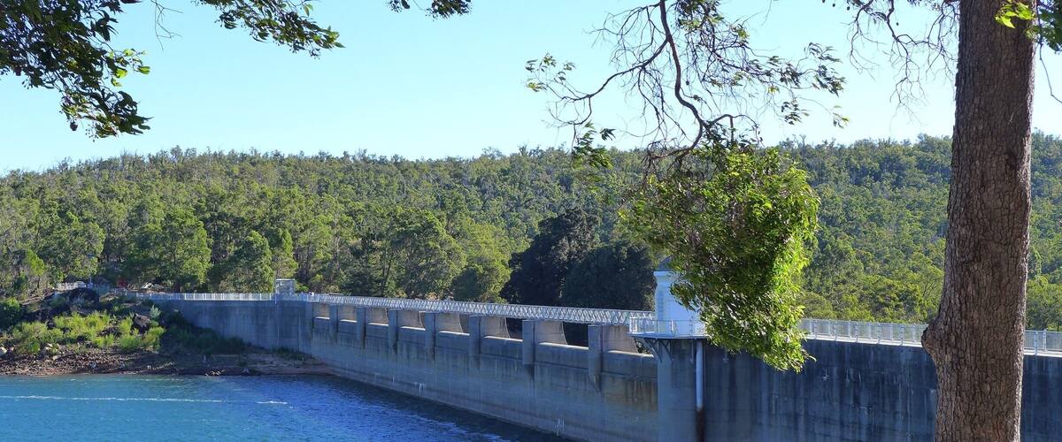 A concrete dam over a river with a forested hillside in the background.