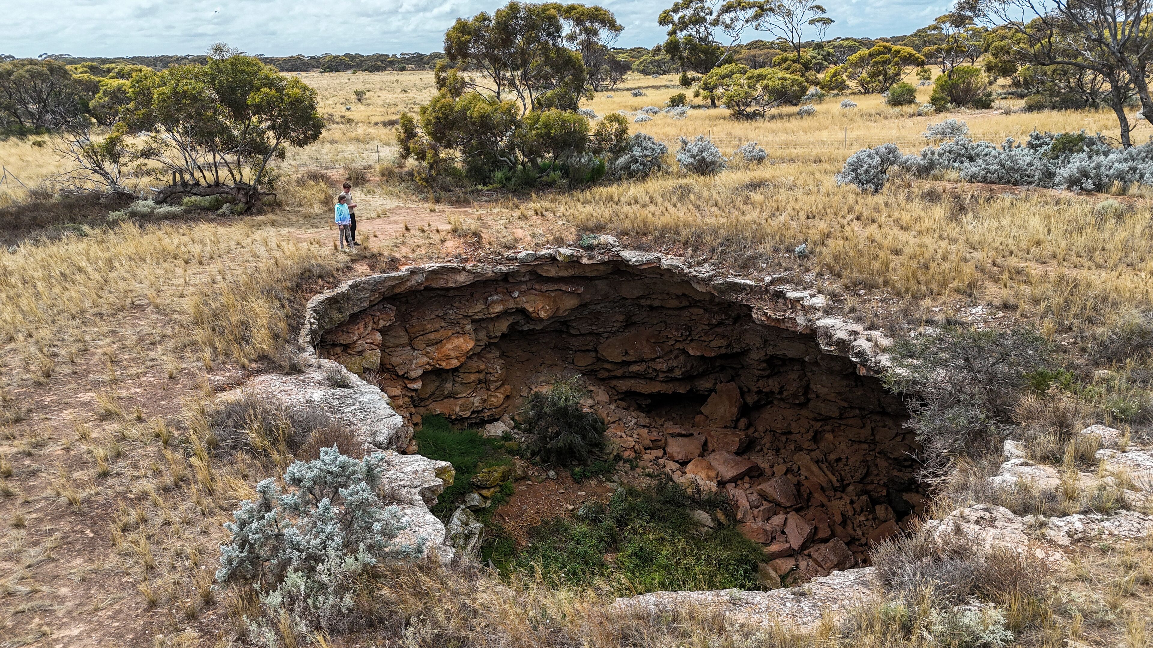 Aerial of two kids looking into a remote sinkhole