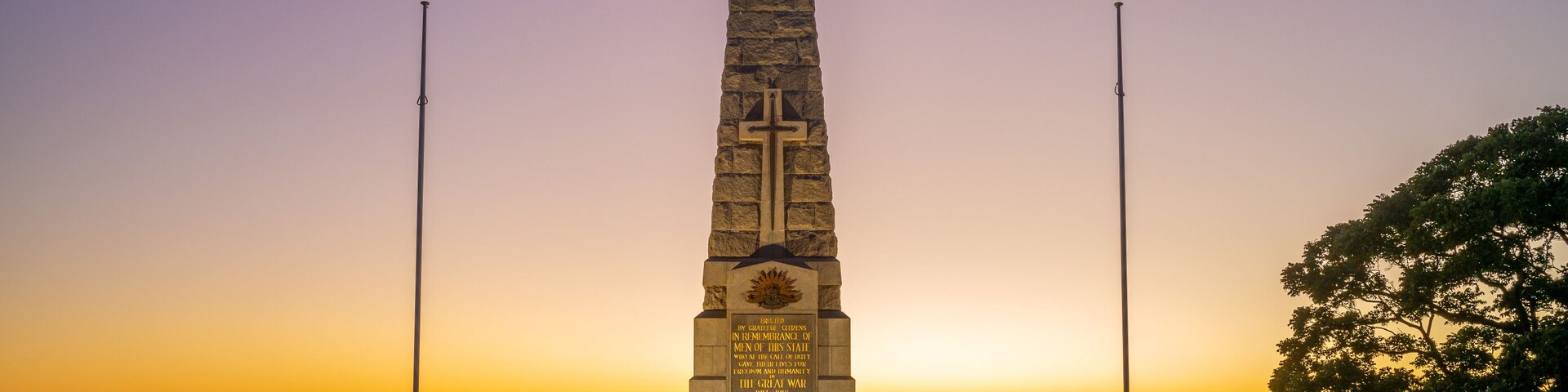 Um monumento alto com uma cruz no topo, cercado por uma cerca branca e degraus que levam até ele.