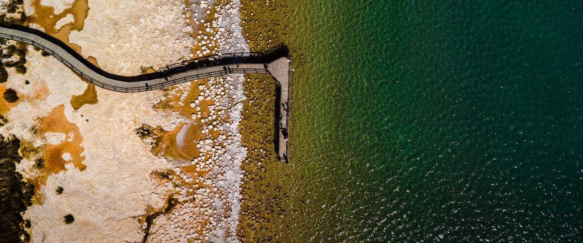An aerial view of a coastal area with a winding road along the beach, clear water, and a sandy shoreline with some vegetation.