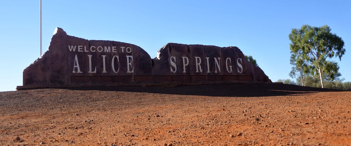 A welcome sign for Alice Springs with a flagpole and a clear blue sky.