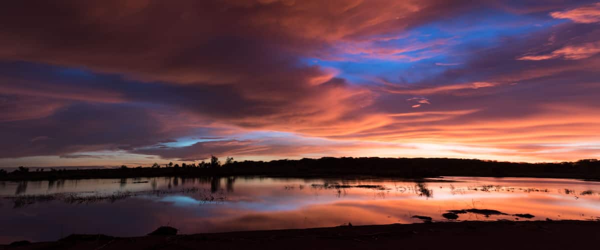 Un coucher de soleil sur un lac paisible, avec des nuages aux couleurs éclatantes.