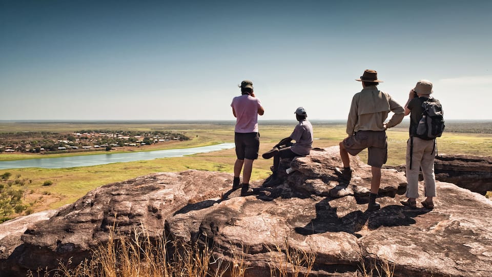 A group of people on a rocky outcrop overlooking a river and distant buildings.