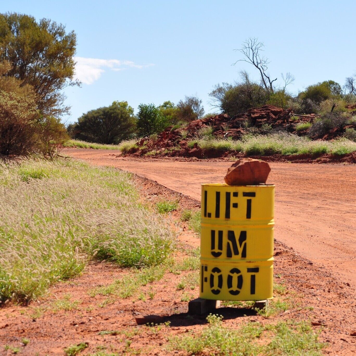 A dirt road with a yellow sign that reads "LIFT UM FOOT".