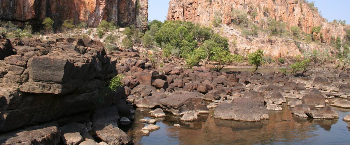 A rocky riverbed with large boulders and cliffs in the background.
