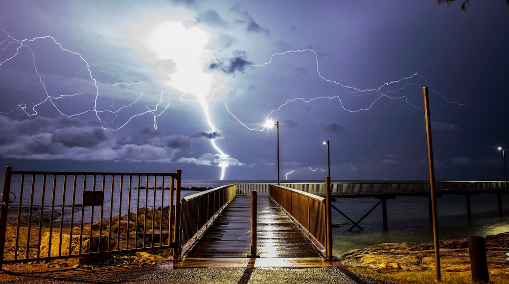 A stormy night with lightning striking near a wooden boardwalk leading to a pier.