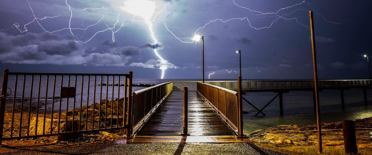 A stormy night with lightning striking near a wooden boardwalk leading to a pier.
