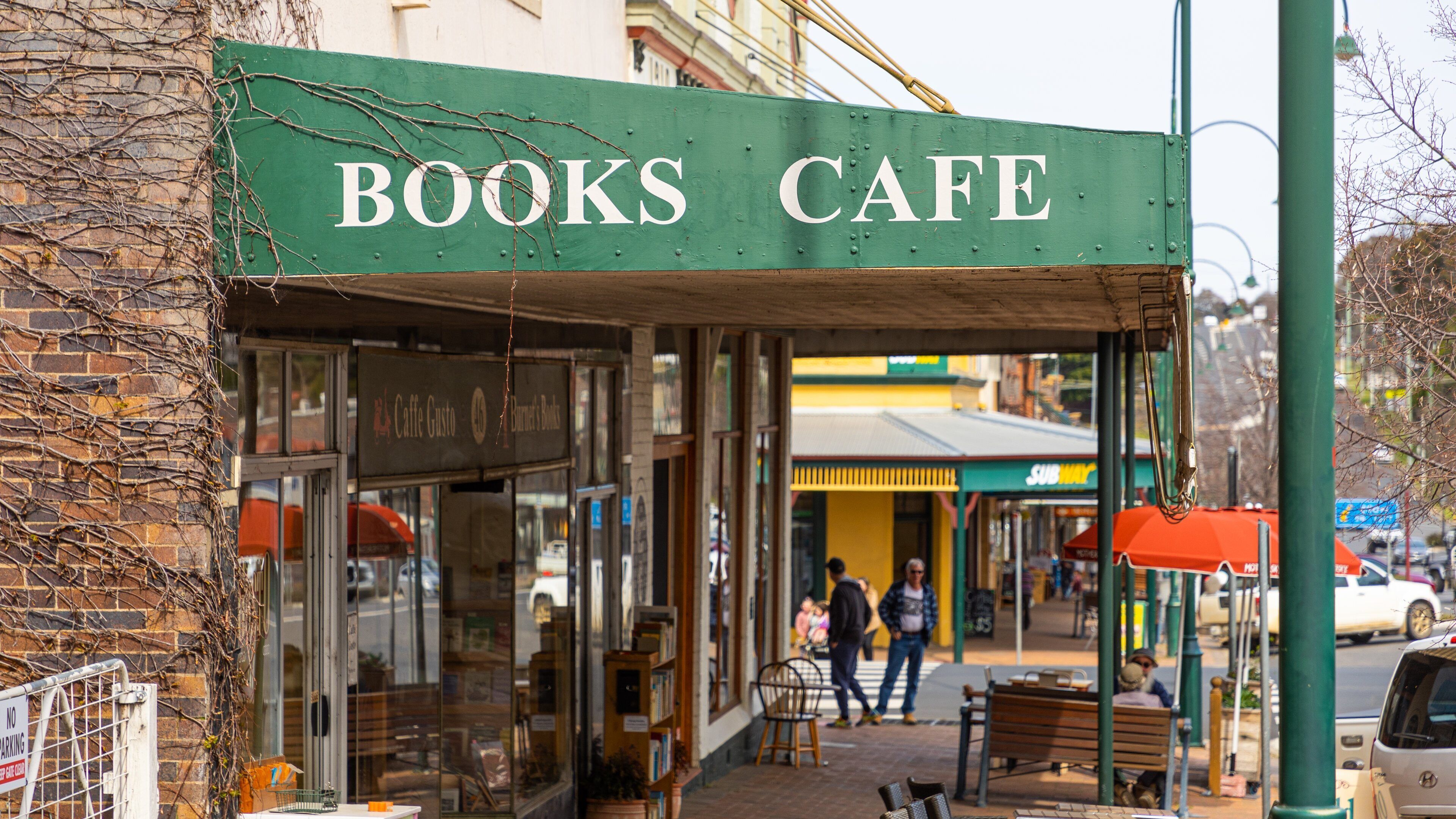 A Books Cafe with a green awning, a brick wall, and a sidewalk with people walking.