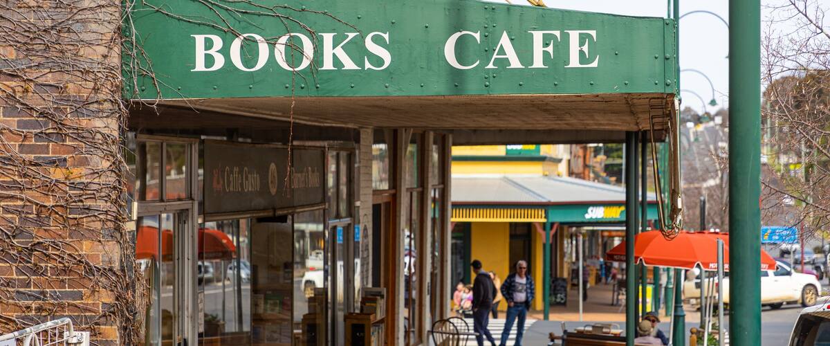 A Books Cafe with a green awning, a brick wall, and a sidewalk with people walking.