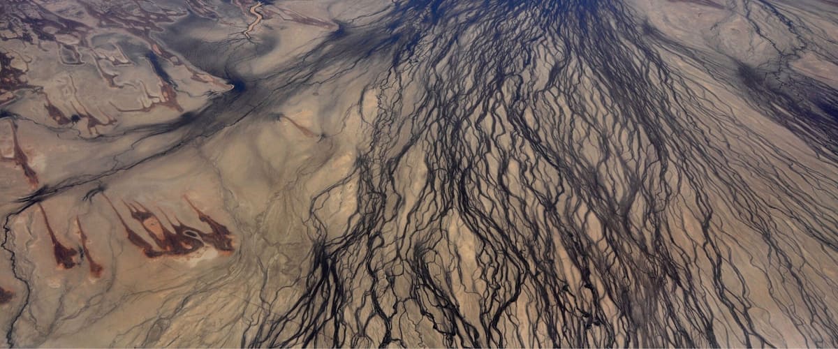 A vast desert landscape with intricate river networks and a prominent mountain range.