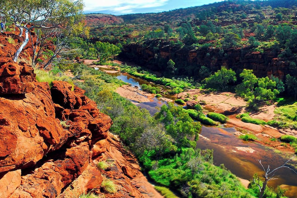 A river flowing through a canyon with red rock formations and green vegetation.