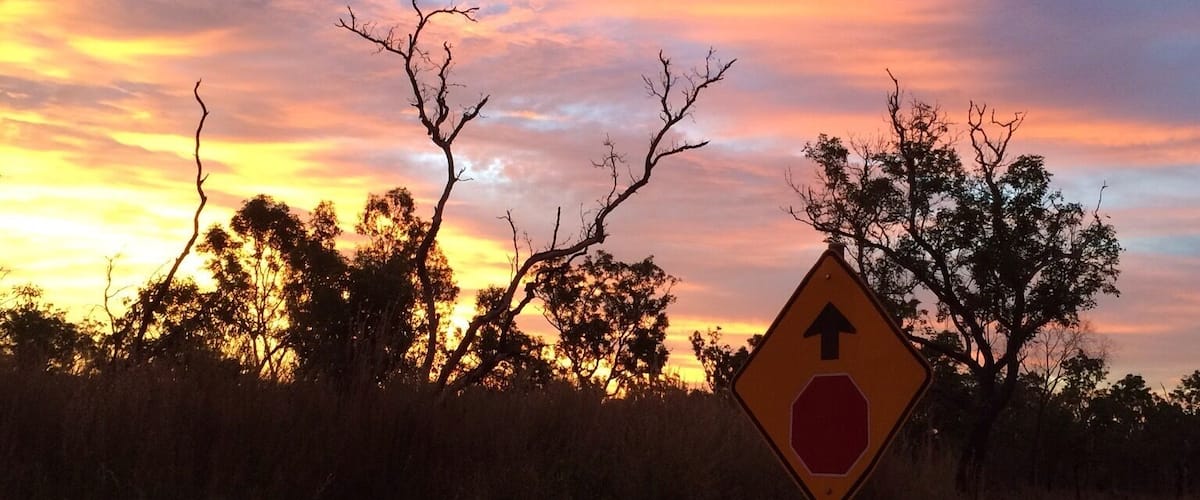A sunset with a road sign indicating a stop ahead.