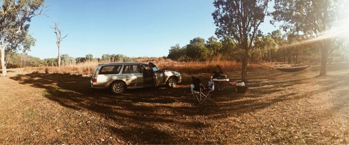 A silver SUV parked in a dry grass field with trees in the background.