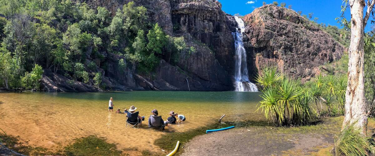 A waterfall, clear water, and people sitting by the water.