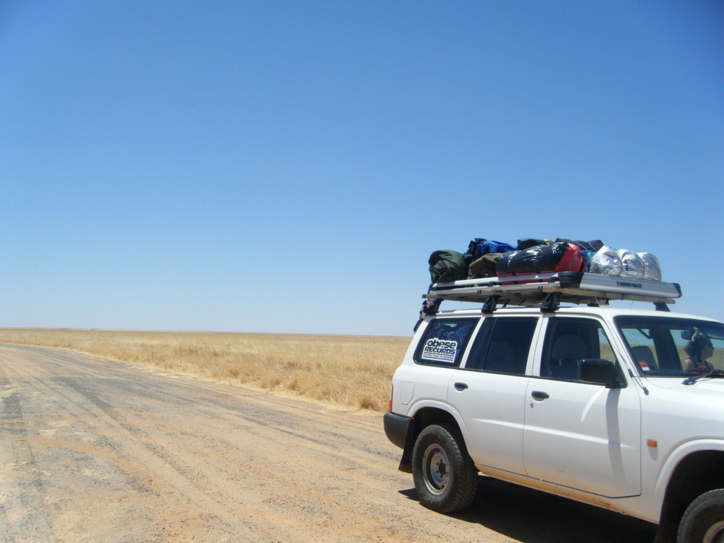 A white SUV parked on a dirt road with luggage on the roof.