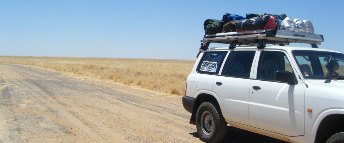 A white SUV parked on a dirt road with luggage on the roof.